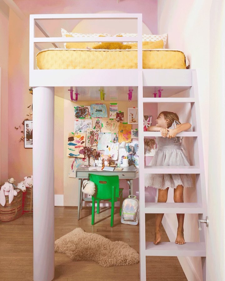 Child climbing white ladder to loft bed in kids room with art wall, desk, and chair, showcasing modern interior design and child-friendly space.