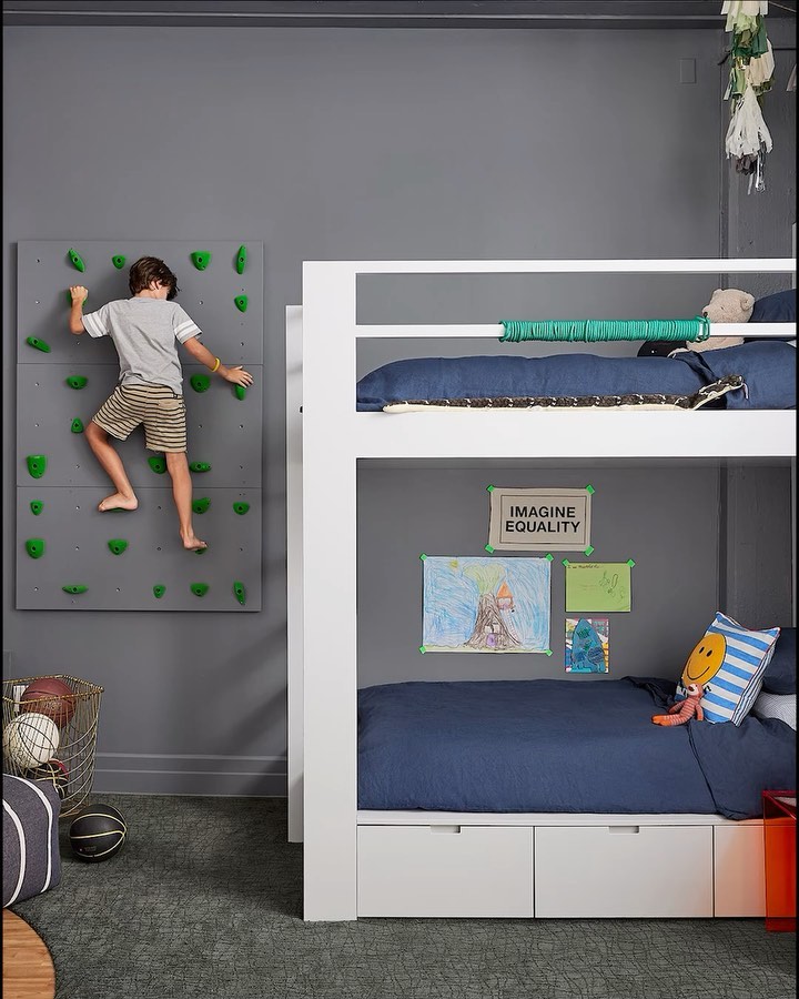 A child climbs a rock wall in a playful bedroom with bunk beds, showcasing an active and creative indoor space designed for kids.
