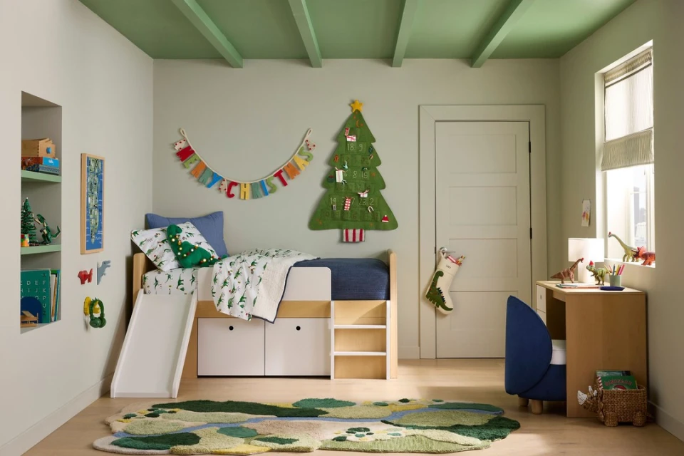 Kids' bedroom with a white bunk bed featuring a slide, complemented by a cozy rug, Christmas decorations, and a desk set. 