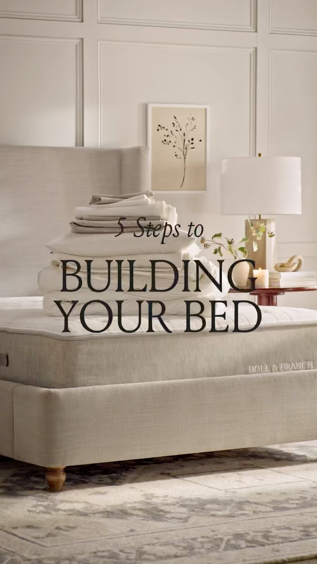 Bedroom interior with a neatly made bed, stacked white linens, a bedside table with a lamp, and neutral tones creating a serene atmosphere.