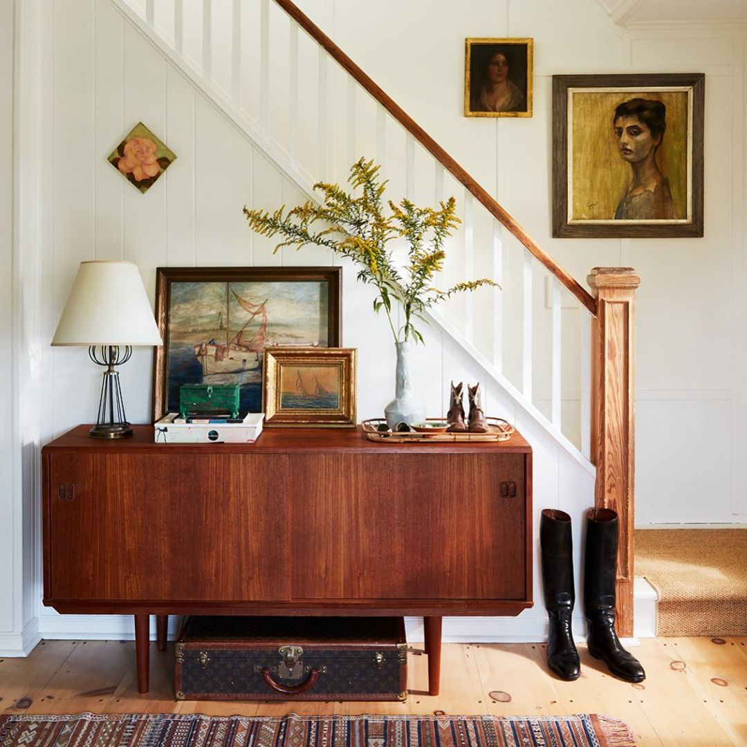 Interior hallway with wood sideboard, paintings, and staircase, creating a vintage and artistic home decor display.