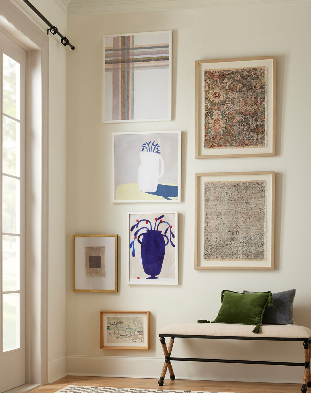 Living room interior featuring a collection of framed art hanging above a wooden bench with decorative pillows, creating a stylish and inviting space.