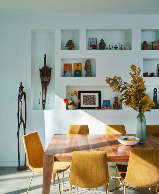 Interior of a dining room with a wood table and yellow chairs, featuring art and decor items displayed in recessed wall niches.