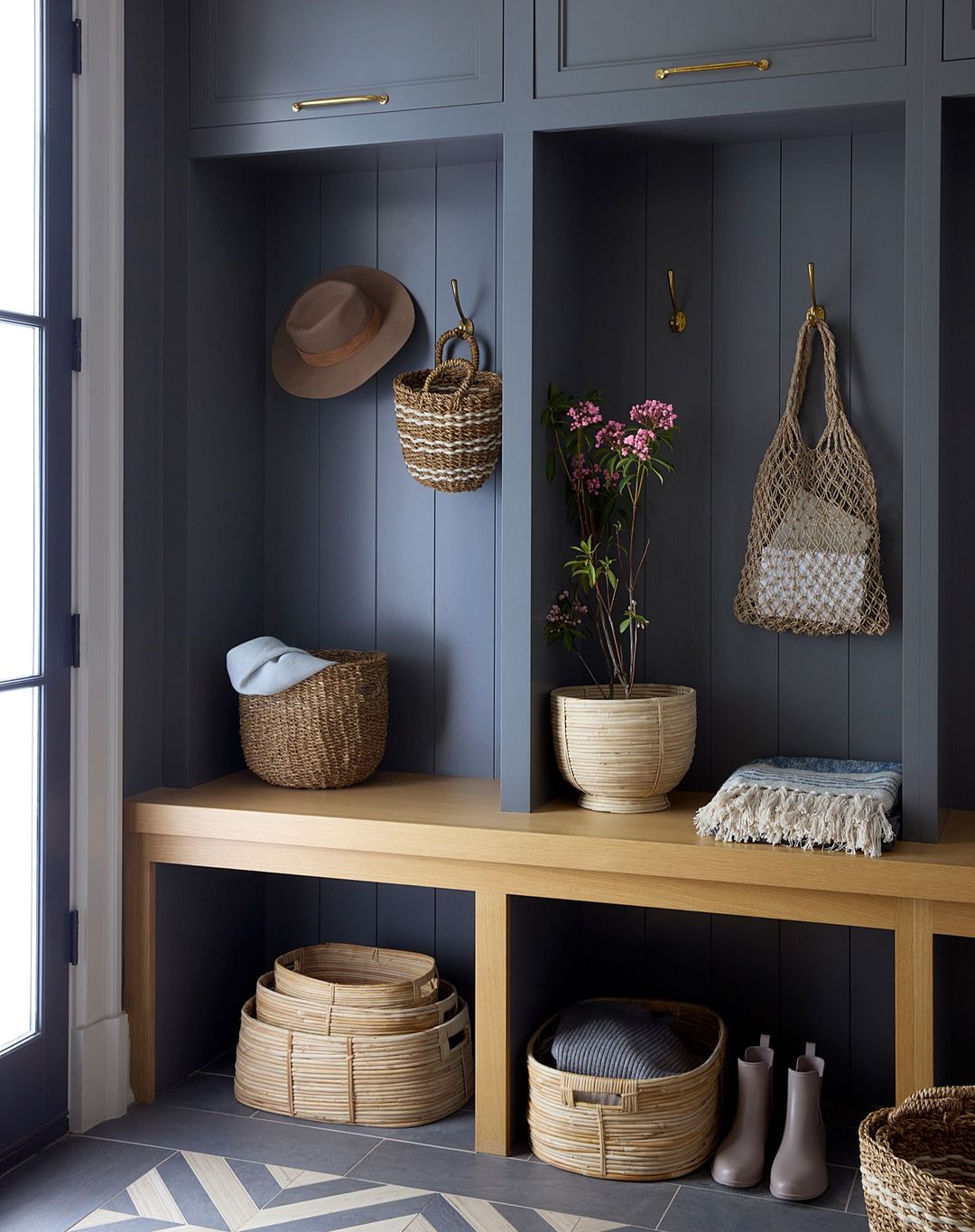 Mudroom interior features built-in storage, wood bench, woven baskets, tile flooring and decor in a stylish home organization design.