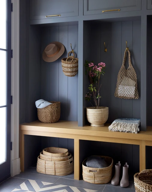 Mudroom interior features built-in storage, wood bench, woven baskets, tile flooring and decor in a stylish home organization design.