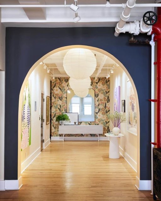 Archway view of a hallway interior with wooden floor, flower-patterned wallpaper, hanging paper lanterns, and wall art.