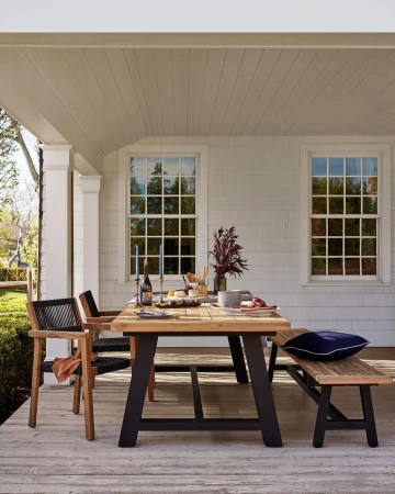 Outdoor dining on a porch featuring a wooden table set with candles, glassware, and decorative elements, creating an inviting atmosphere.