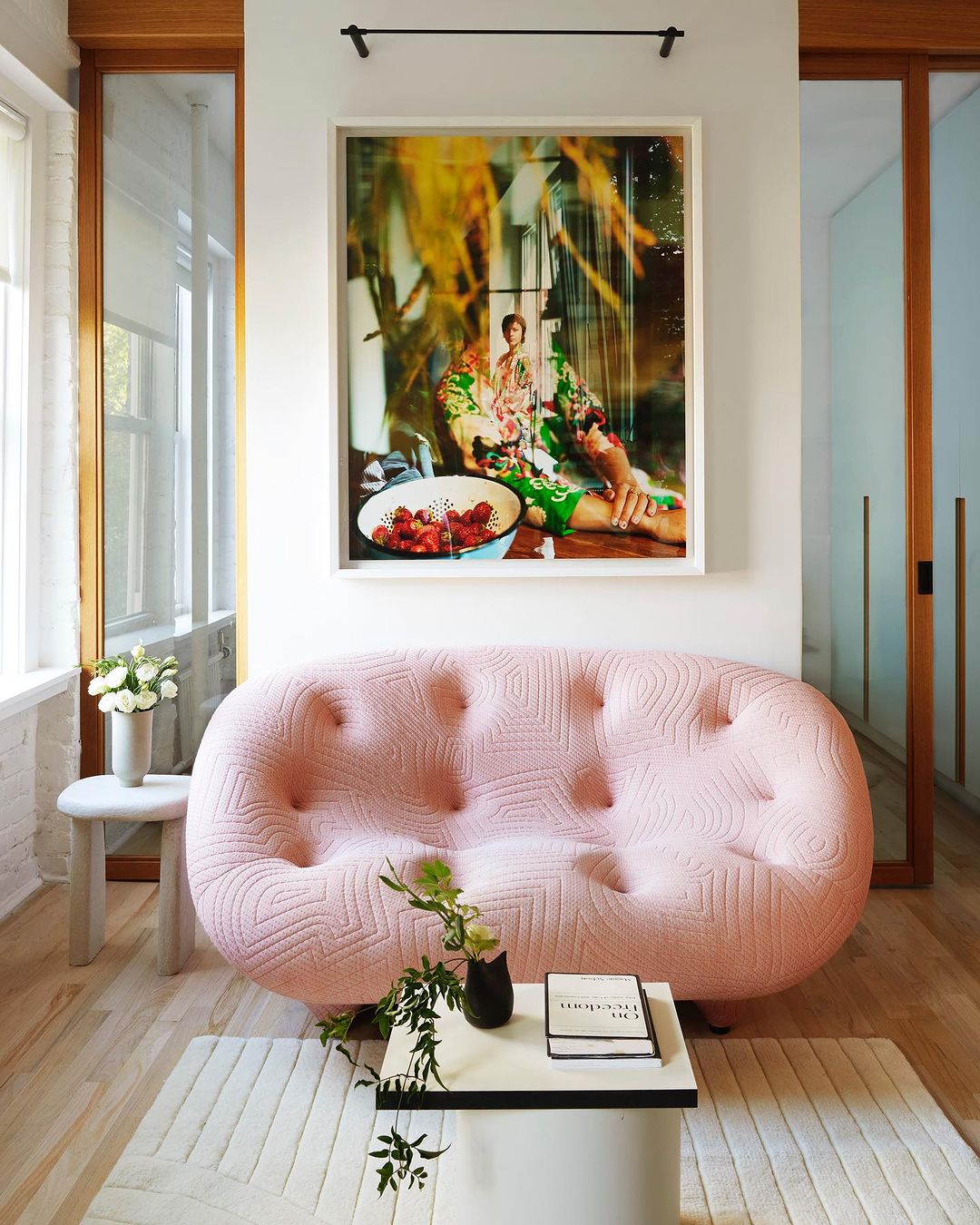 Interior design featuring a pink tufted sofa, a modern coffee table, and an art print in a bright, stylishly decorated living room.