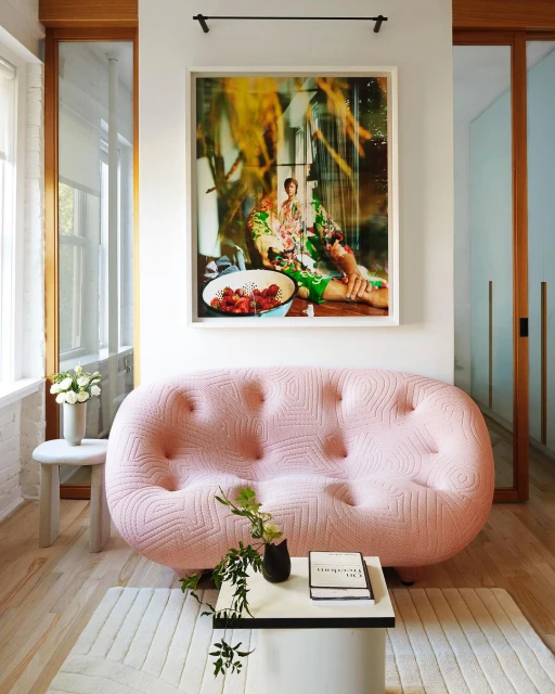 Interior design featuring a pink tufted sofa, a modern coffee table, and an art print in a bright, stylishly decorated living room.