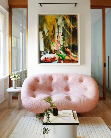 Interior design featuring a pink tufted sofa, a modern coffee table, and an art print in a bright, stylishly decorated living room.