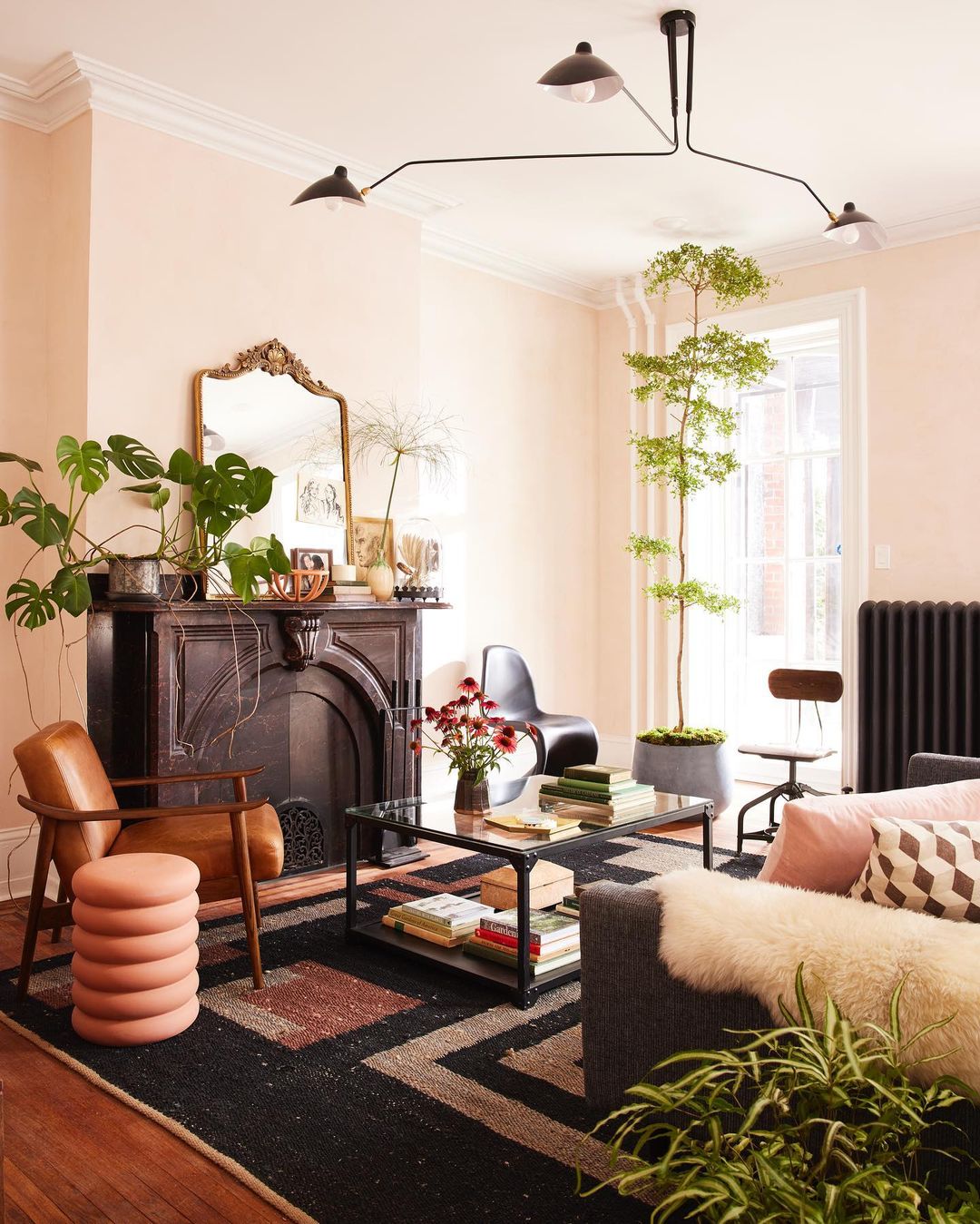 Living room interior featuring a black fireplace, patterned rug, brown leather chair, and decorative plants in a cozy, stylish setting.