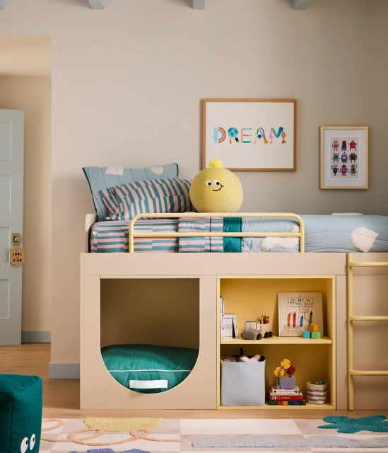 Child's bedroom with a raised bed, colorful bedding and decorative pillows, artwork, and a cozy play area underneath the bed.
