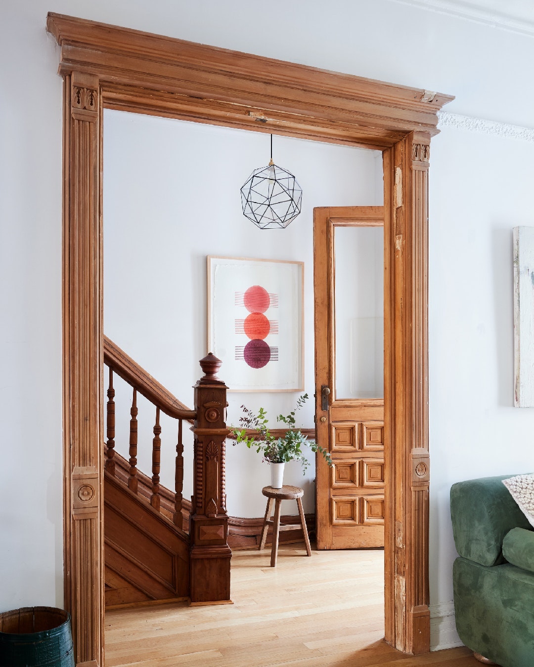Interior view through an ornate doorway into a home featuring stairs, an artwork with red circles, and a geometric pendant light fixture.