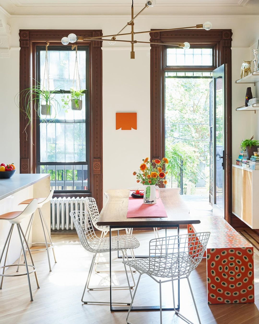 A bright and airy dining room interior features a light wood dining table with modern wire chairs and a decorative light fixture above.