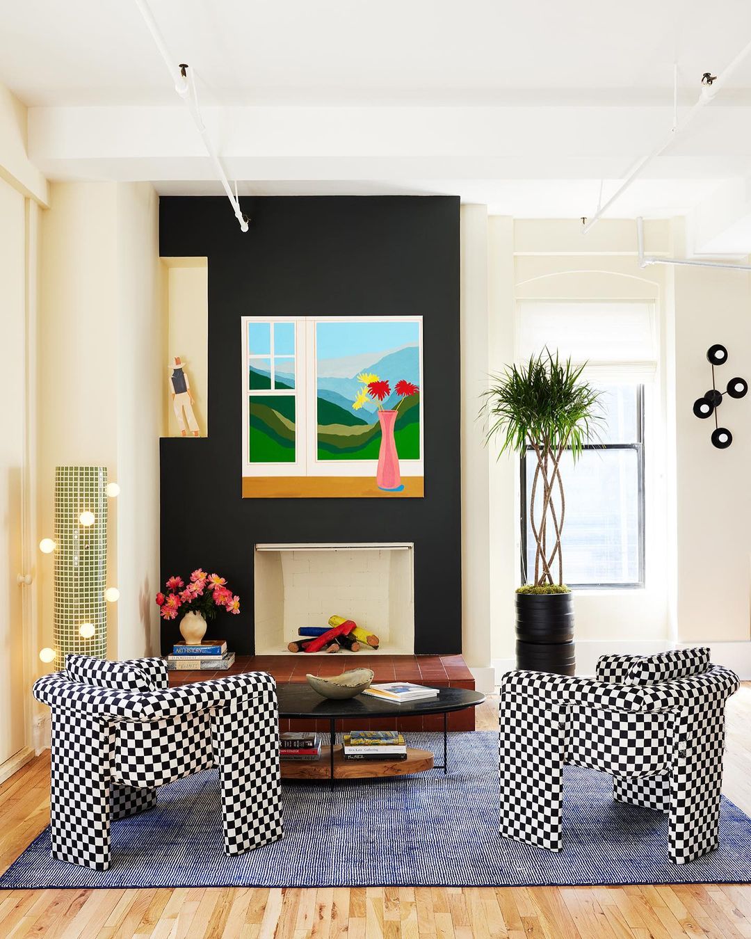 Living room interior with two black and white checkered chairs, a blue rug, and a landscape painting on a black accent wall.