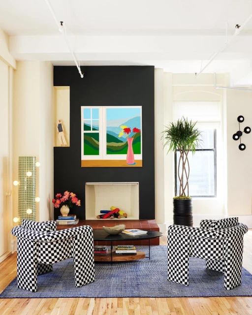 Living room interior with two black and white checkered chairs, a blue rug, and a landscape painting on a black accent wall.