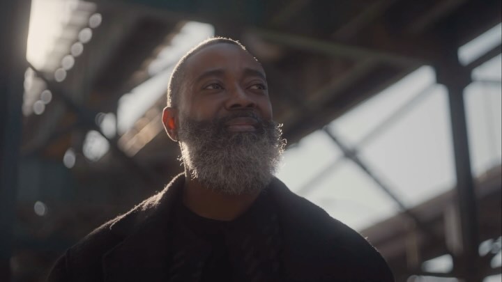 Close-up portrait of a mature African-American man with a salt-and-pepper beard, looking up and away, in an industrial interior.