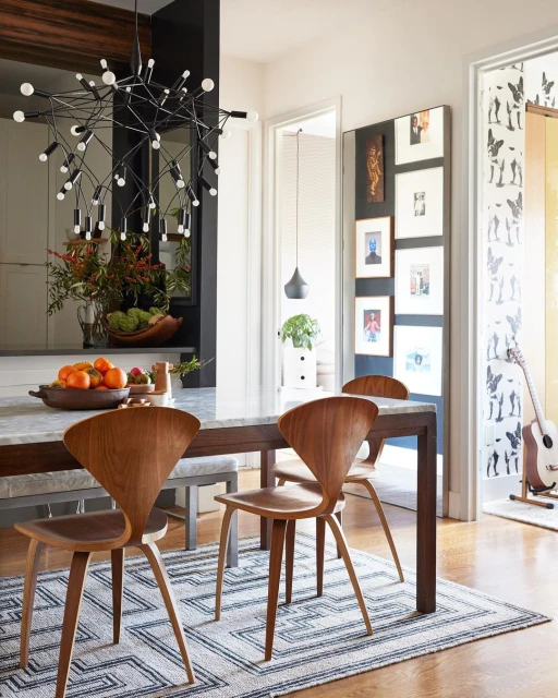 Dining room interior with wood chairs around a marble table, a modern chandelier, and black and white patterned rug on hardwood floor.