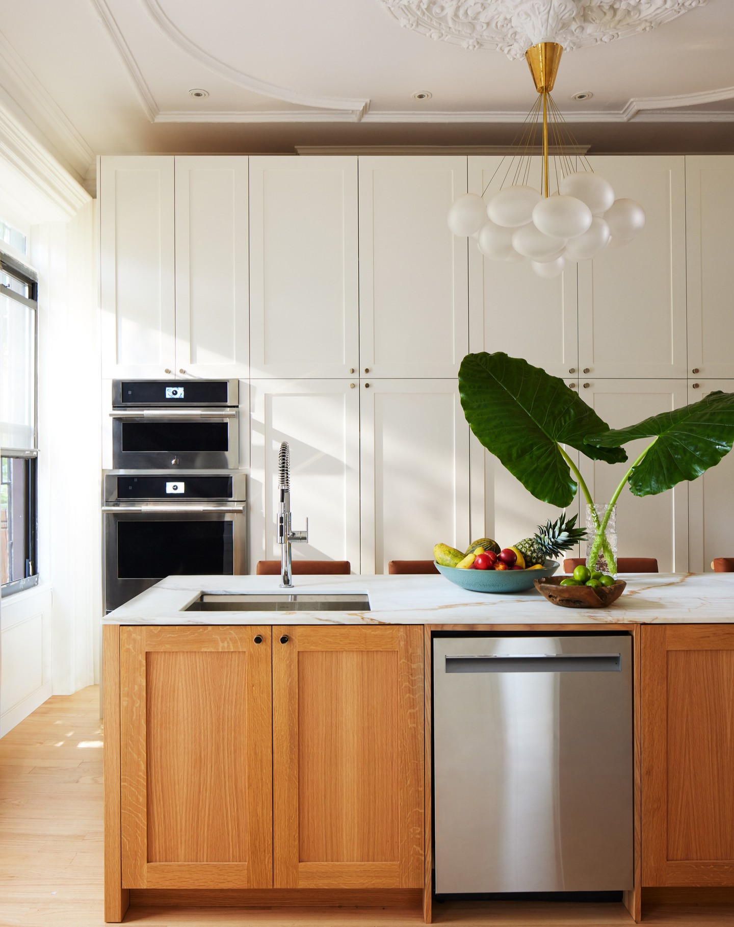 Bright, modern kitchen interior with white cabinets, marble countertops, wooden island, stainless steel appliances, and vibrant fruit.