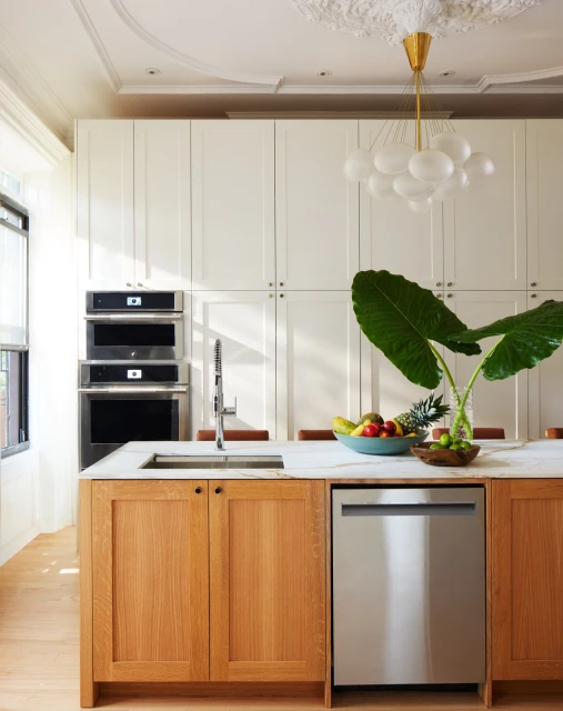 Bright, modern kitchen interior with white cabinets, marble countertops, wooden island, stainless steel appliances, and vibrant fruit.