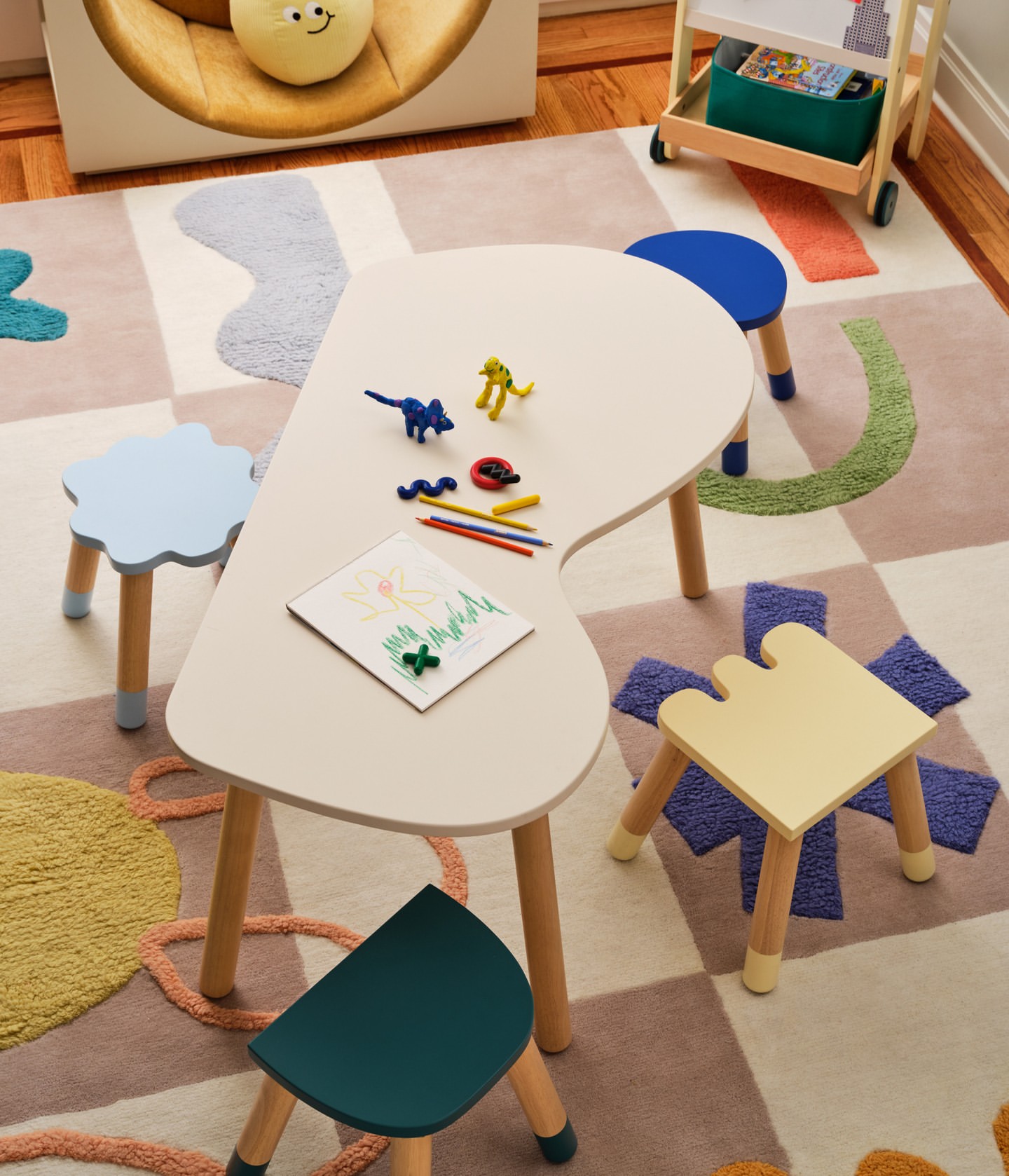 Child's playroom featuring a white table with colorful chairs, artwork, and toys on a patterned rug, creating a fun and inviting space.