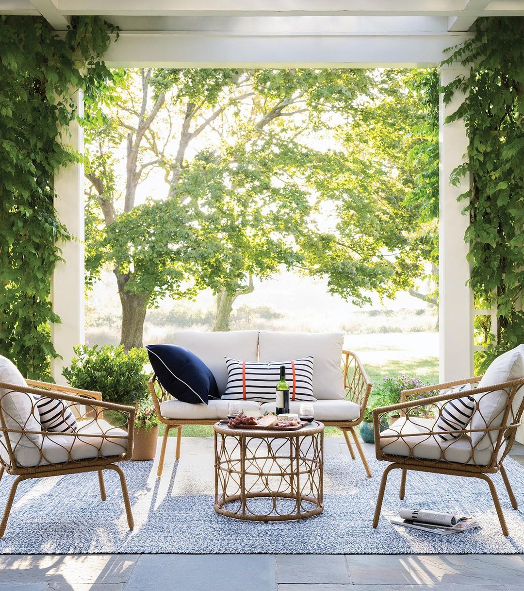 Outdoor seating area with rattan chairs, loveseat, and round table on a patio, framed by columns and lush greenery.