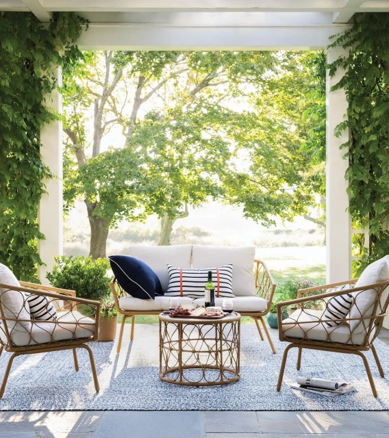 Outdoor seating area with rattan chairs, loveseat, and round table on a patio, framed by columns and lush greenery.
