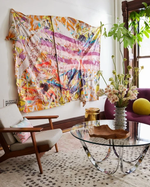 Living room interior featuring an abstract textile wall hanging, modern furniture, and plants in natural light.