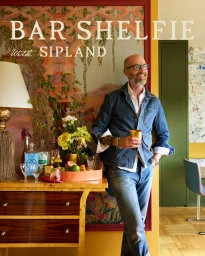 A mature man in glasses and a denim shirt holding a gold cup near a stylish bar cart by photographer David Land