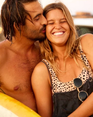 Close-up portrait of a man kissing a laughing woman on the cheek while outdoors