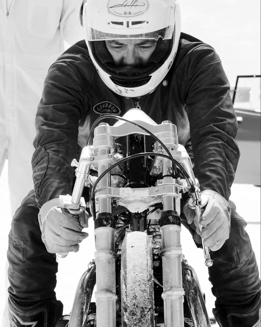 Monochrome shot of a man in a helmet and racing suit riding a motorcycle, focusing on the details of the bike and rider on the track.