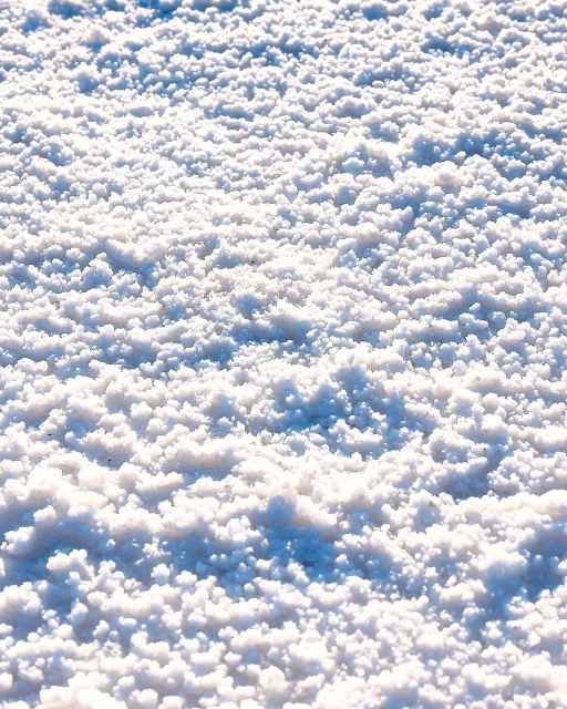 Close-up view of white salt crystals creating a textured landscape-like scene on a sunny day, ideal for backgrounds or abstract visuals.