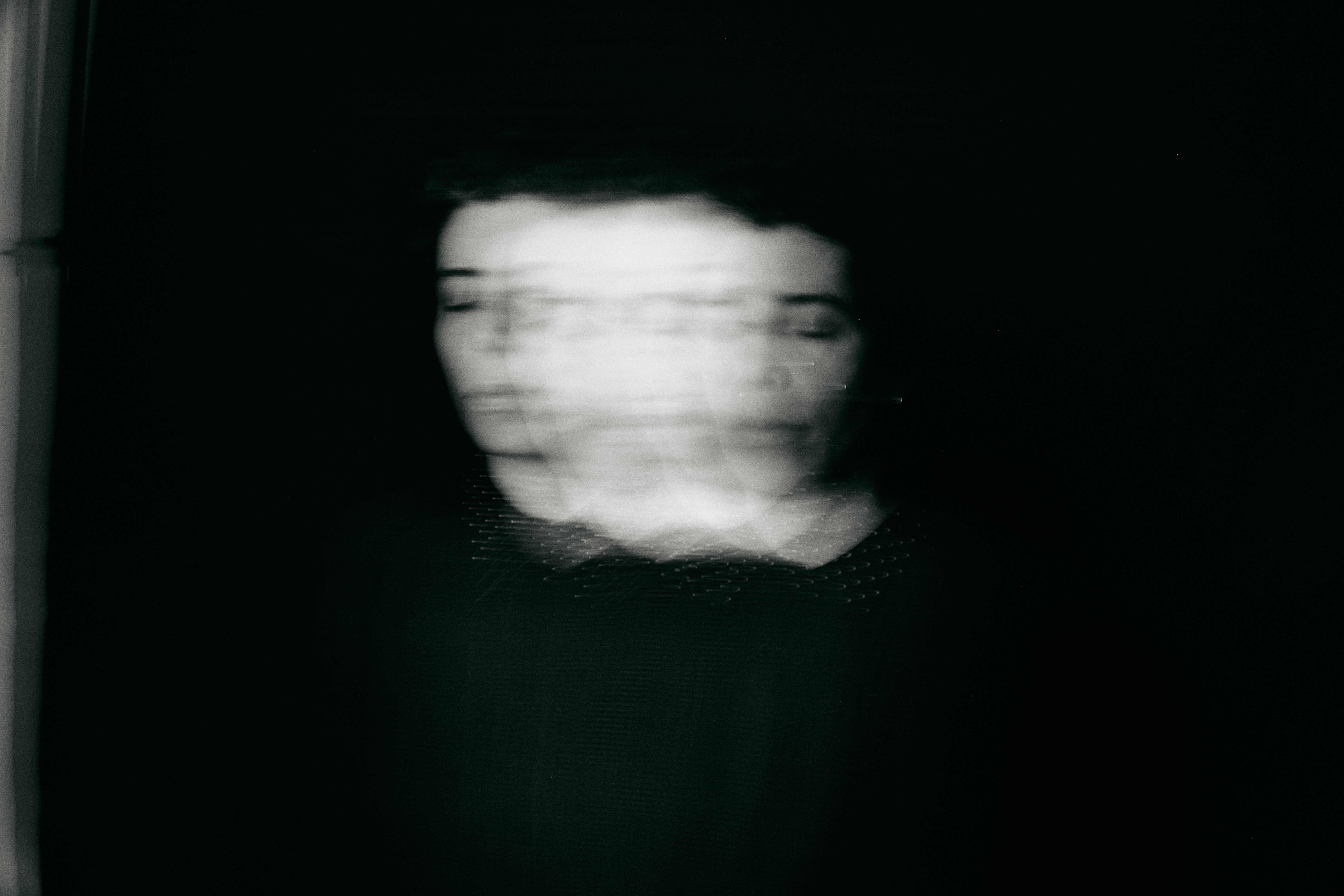 Monochromatic portrait of a woman with a blurred, ethereal quality, set against a dark background creating a ghostly and surreal visual effect.