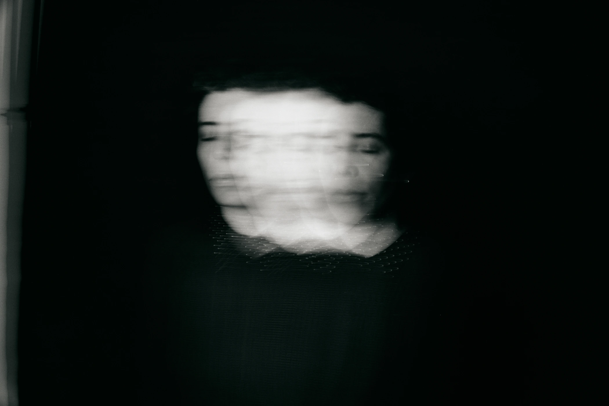 Monochrome portrait of a person with blurred motion effect creating multiple overlapping faces against a dark background.