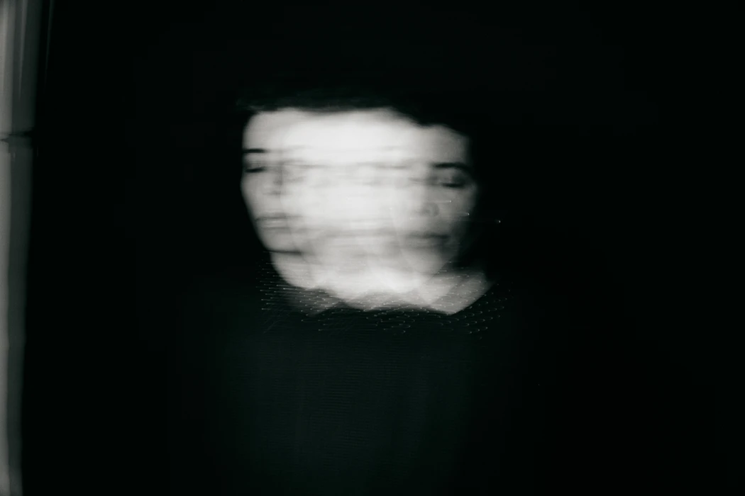 Monochrome portrait of a person with blurred motion effect creating multiple overlapping faces against a dark background.