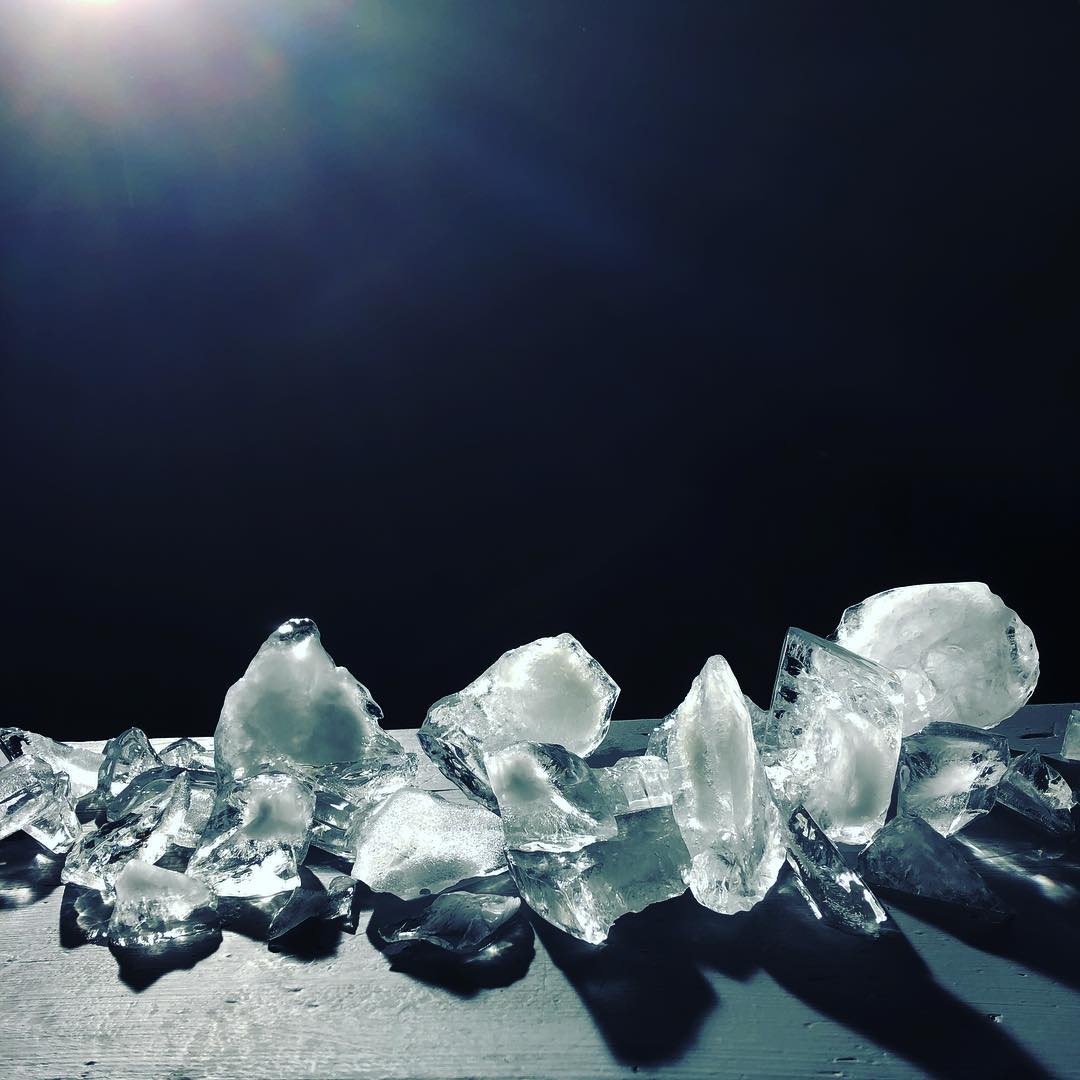 A collection of irregularly shaped clear ice chunks illuminated against a dark background, showcasing a play of light and shadow.