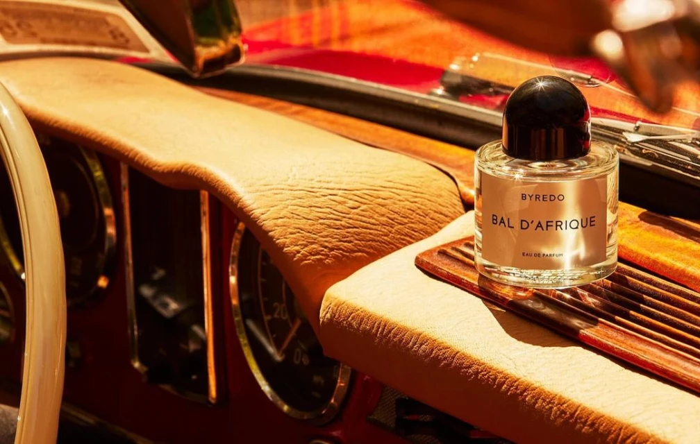 Byredo Bal d'Afrique perfume bottle sits on the dashboard of a vintage car, highlighting luxury and automotive elegance.
