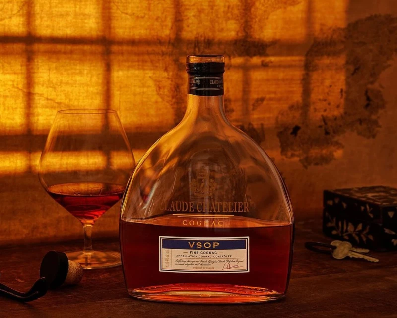 Cognac still life: A bottle of VSOP Cognac and a glass of cognac sit on a wooden table against an amber-lit background.