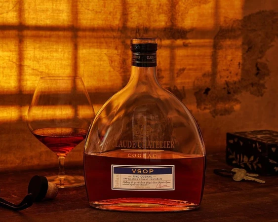 Cognac still life: A bottle of VSOP Cognac and a glass of cognac sit on a wooden table against an amber-lit background.