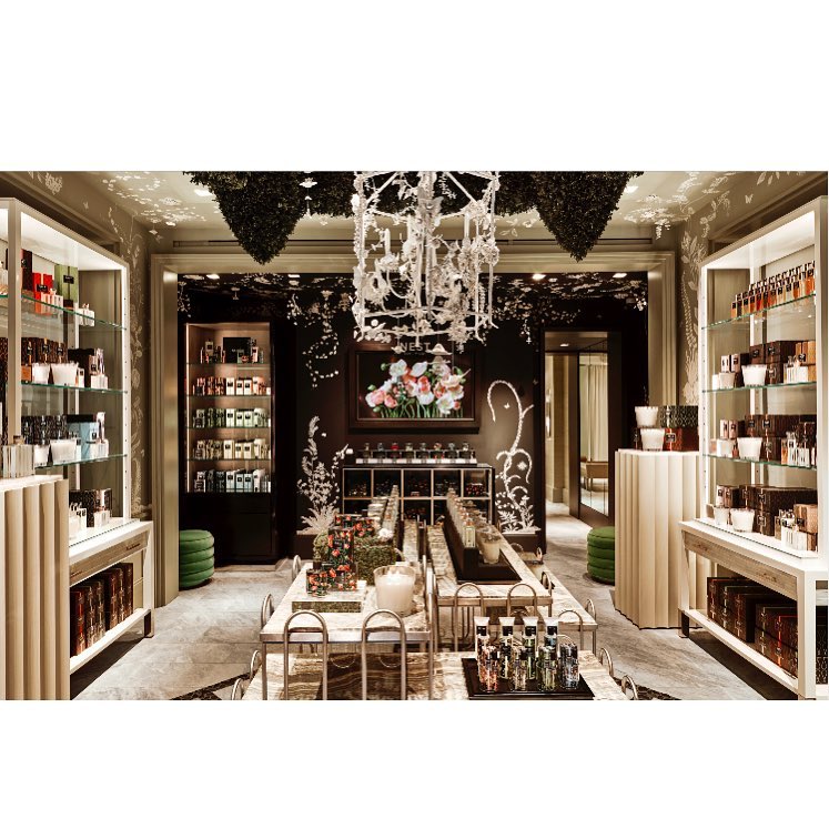 Elegant perfume store interior with display shelves and a central table showcasing various perfume bottles, lit by a decorative chandelier.