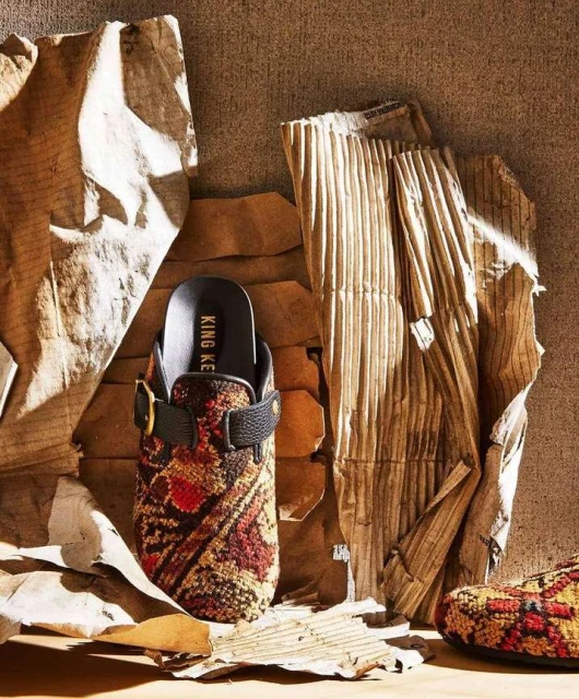 Clog-style shoe with an intricate pattern on display with corrugated and crumpled brown paper providing a visually textured backdrop.