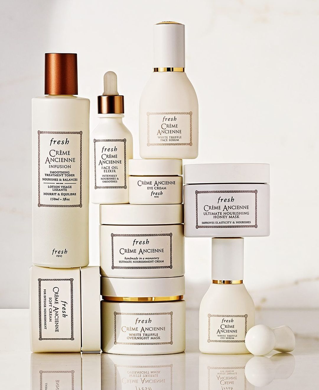 A collection of Fresh Crème Ancienne skincare products are stacked against a light backdrop showcasing the brand's luxury aesthetic.