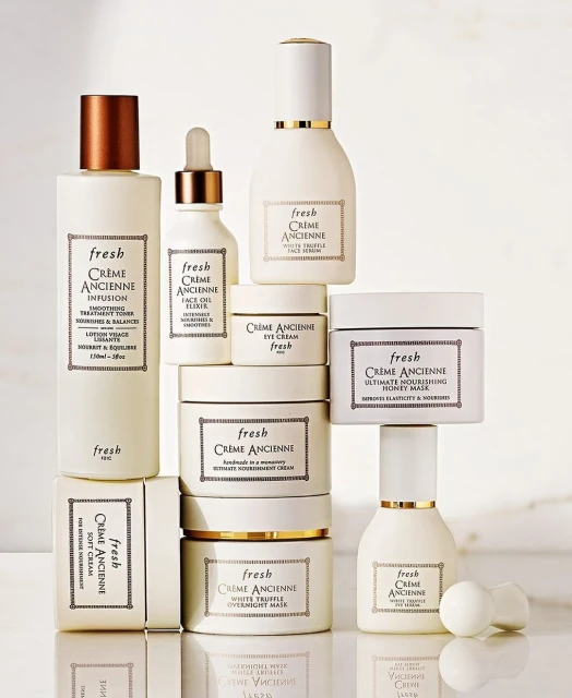 A collection of Fresh Crème Ancienne skincare products are stacked against a light backdrop showcasing the brand's luxury aesthetic.