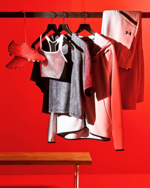 Sports apparel and red cleats hang on a rack against a vibrant red wall, complemented by a wooden bench, creating a dynamic visual.