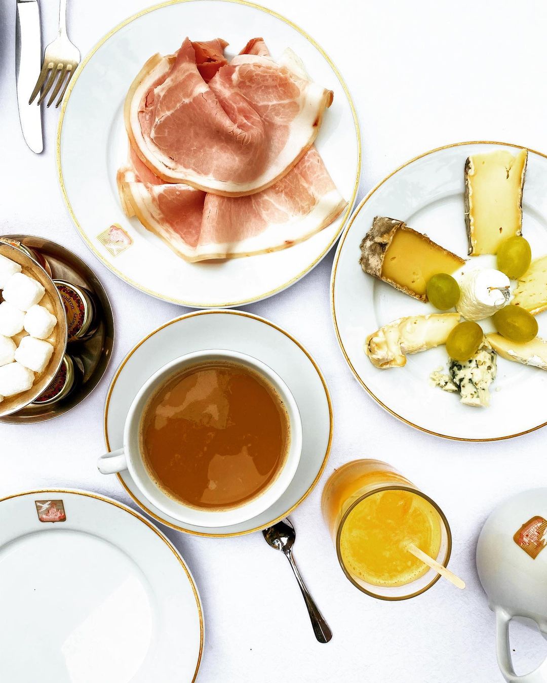 Overhead shot of charcuterie, cheese plate, orange juice, and coffee served on a white table with gold trim for a luxurious meal.