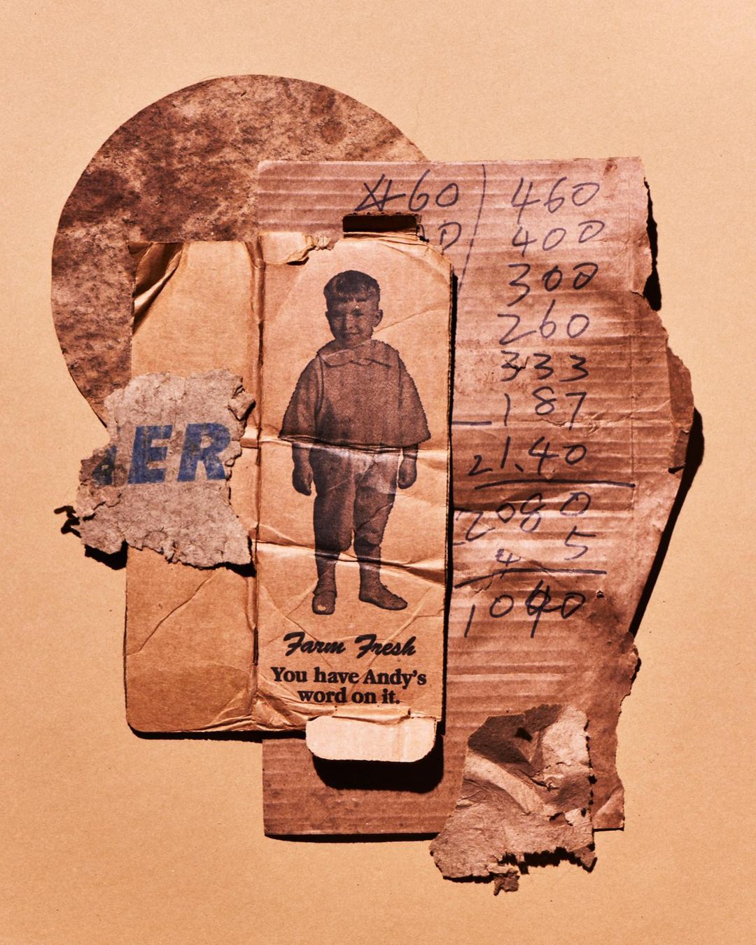 Collage of cardboard fragments with a boy's vintage photo, overlaid on a round piece, against a plain, light beige background.