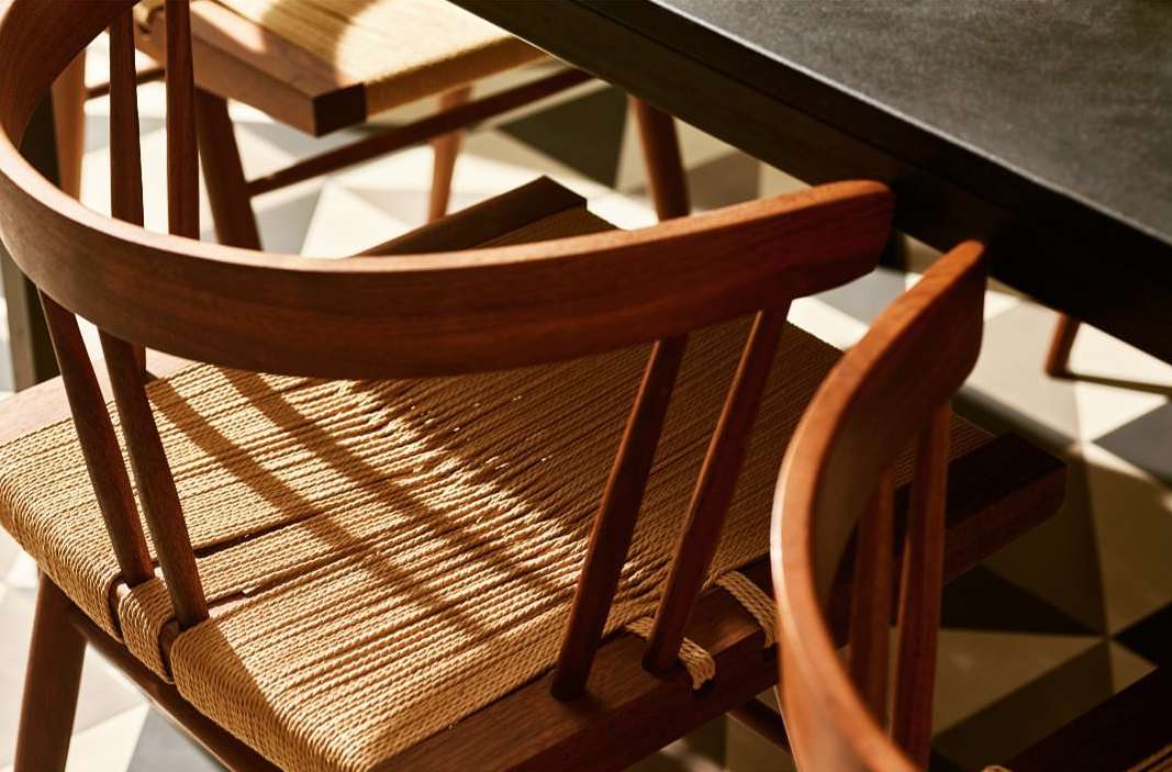 Close-up of dark-stained wood dining chairs with woven seats, arranged on a geometric tiled floor next to a black tabletop.