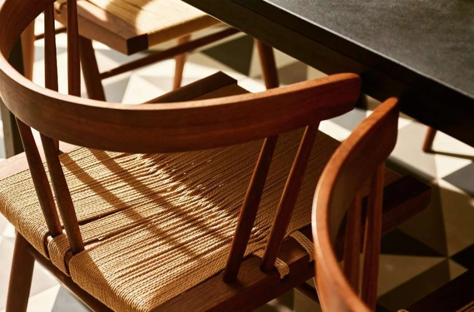 Close-up of dark-stained wood dining chairs with woven seats, arranged on a geometric tiled floor next to a black tabletop.