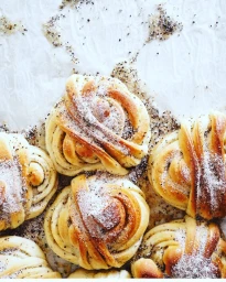 Close-up overhead shot of twisted baked sweet buns dusted with sugar and dark spices on white paper.