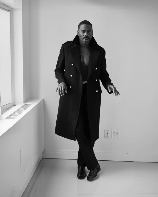 A black and white full-length portrait of a handsome adult male in a black coat, vest, pants and patent-leather shoes, posing indoors.